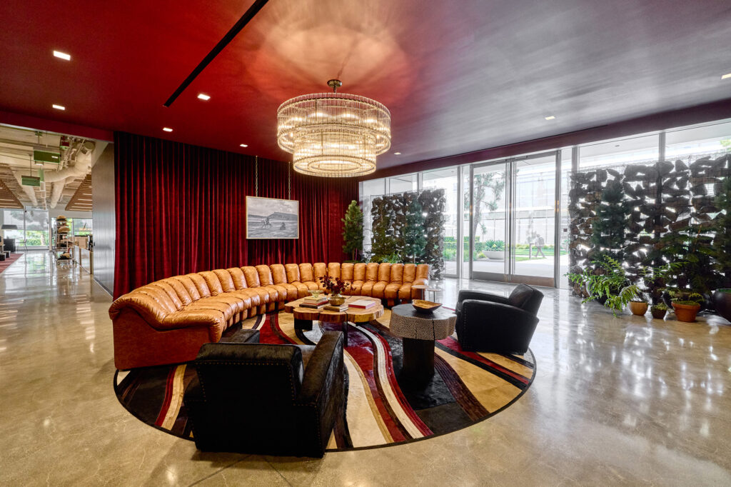 Common area lounge space inside Boot Barn's corporate headquarters, featuring a large sofa with chairs, red ceiling and drapes, and a large light fixture.